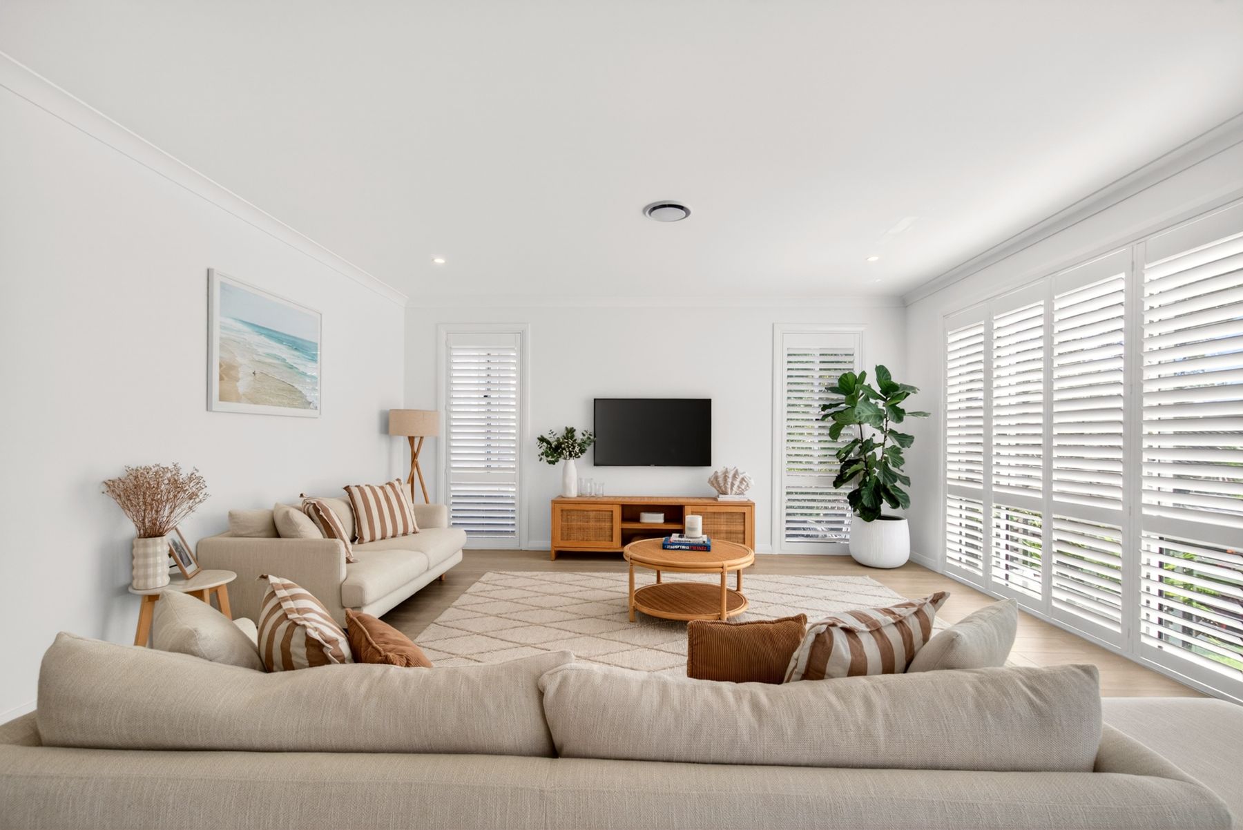 Bright coastal living room with linen sofas, striped cushions, a rattan coffee table and white plantation shutters