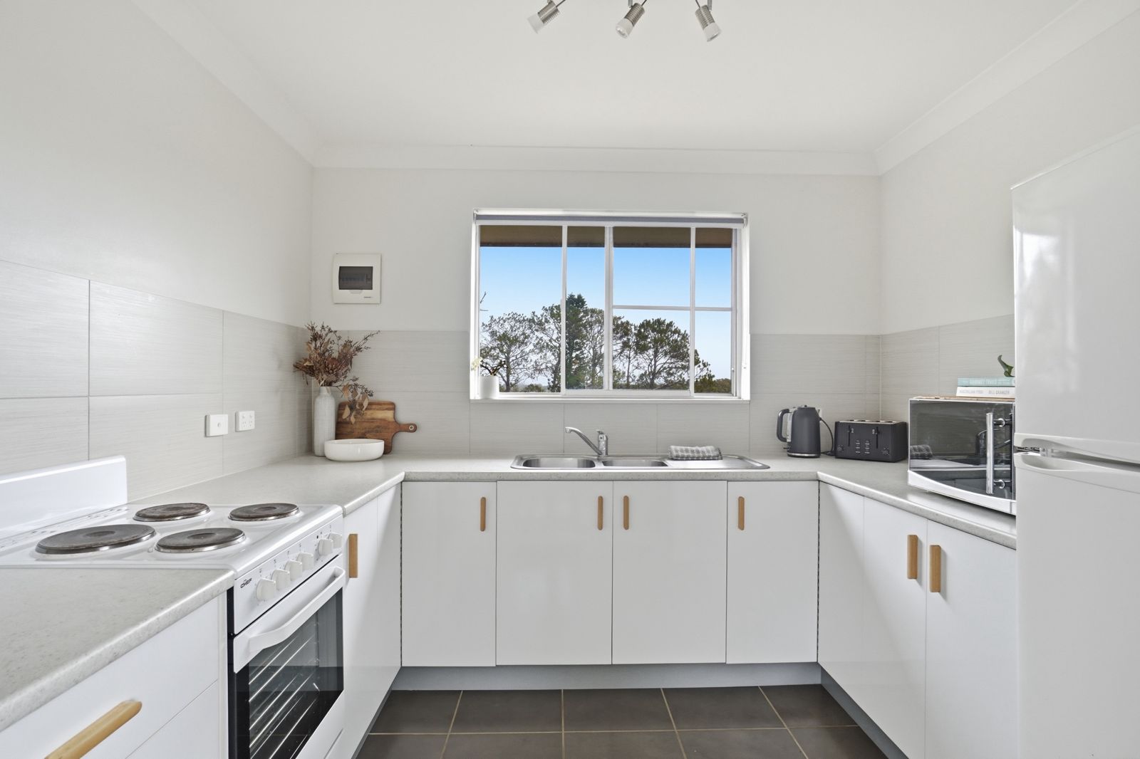 Simple white short-stay kitchen with a window view, a timber board and a dried flower arrangement