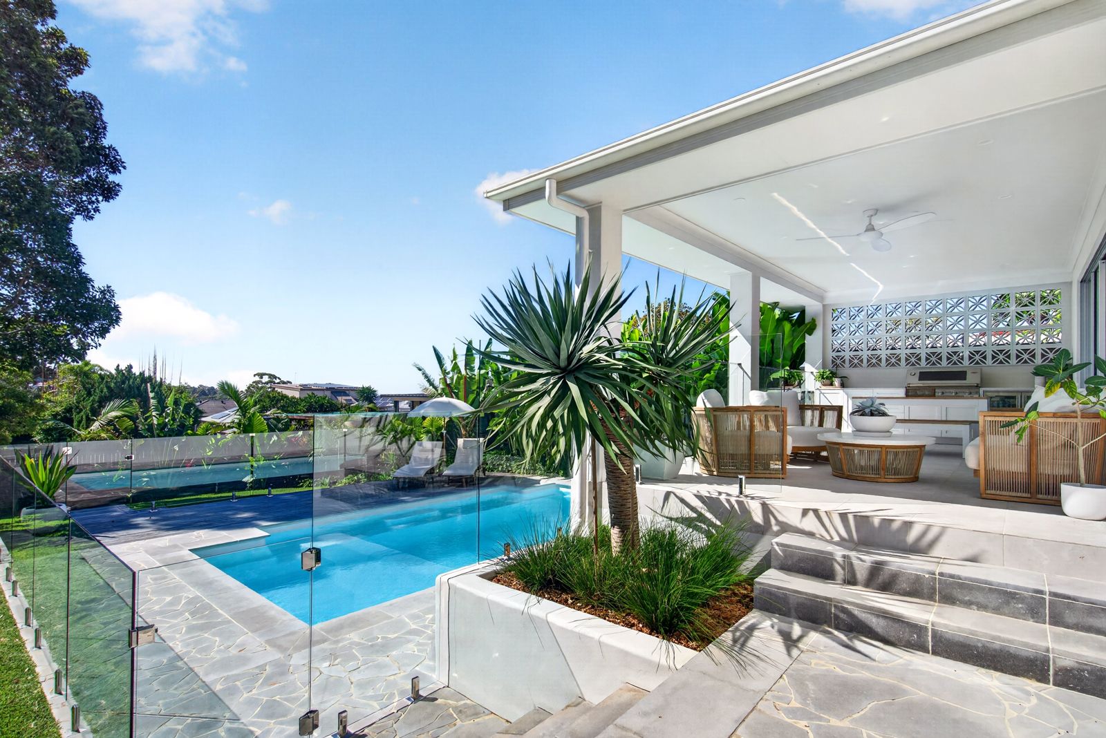 Covered outdoor entertaining area with a pool, rattan lounge chairs, built-in barbecue and tropical planting